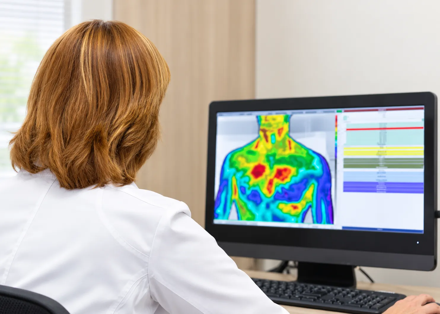 A thermography technician reviewing an infrared thermal image at a clinical workstation